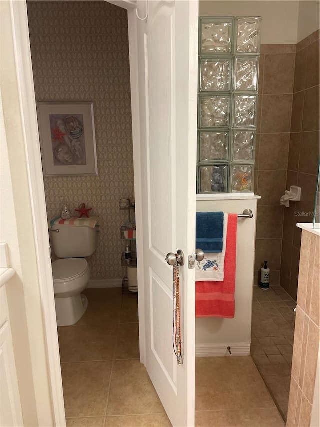 bathroom with toilet, tiled shower, and tile patterned flooring