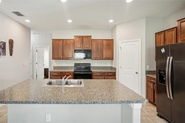 kitchen with black appliances, sink, a kitchen island with sink, light stone counters, and light tile patterned floors