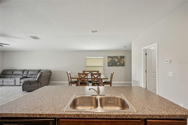 kitchen with ceiling fan, sink, a textured ceiling, and an island with sink