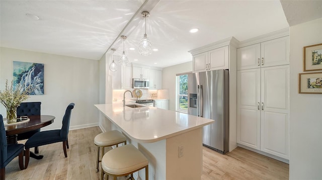 kitchen featuring appliances with stainless steel finishes, light hardwood / wood-style flooring, hanging light fixtures, and white cabinets