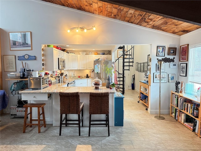 kitchen with white cabinets, lofted ceiling, stainless steel appliances, a kitchen breakfast bar, and wooden ceiling