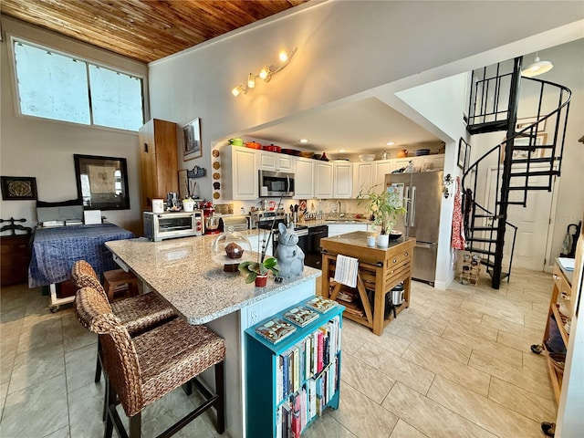 kitchen with light stone countertops, appliances with stainless steel finishes, wood ceiling, a kitchen island, and a kitchen breakfast bar