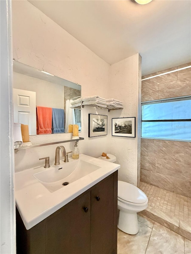 bathroom with toilet, vanity, tile patterned floors, and tiled shower