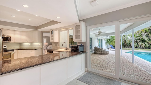 kitchen featuring ceiling fan, sink, appliances with stainless steel finishes, white cabinets, and dark stone counters