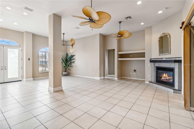 unfurnished living room with a tile fireplace, built in features, light tile patterned floors, ceiling fan, and french doors