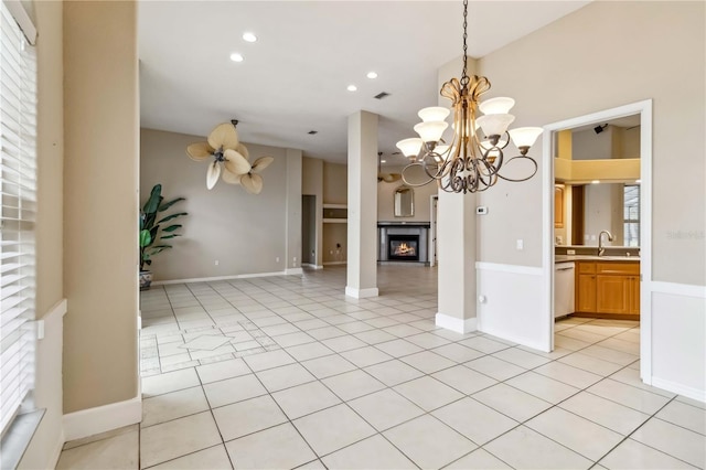 interior space with light tile patterned flooring, white dishwasher, hanging light fixtures, ceiling fan with notable chandelier, and sink