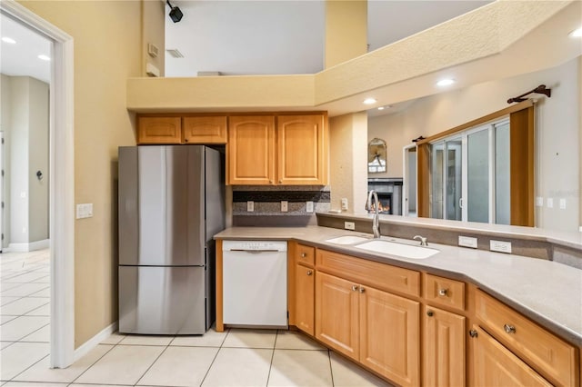 kitchen featuring a towering ceiling, sink, white dishwasher, light tile patterned floors, and stainless steel fridge