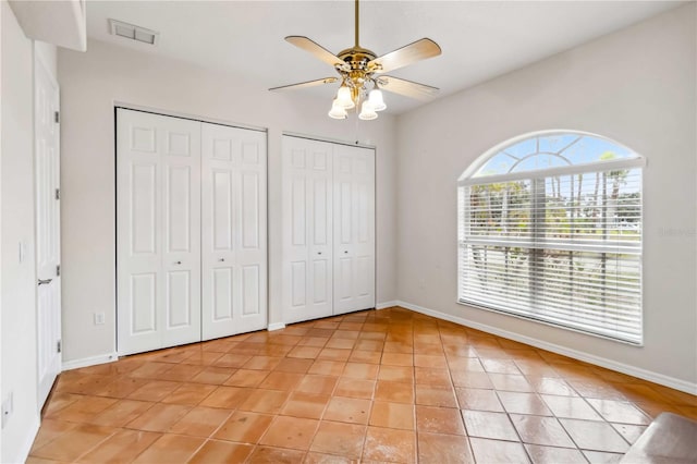 unfurnished bedroom featuring multiple closets, ceiling fan, and light tile patterned floors