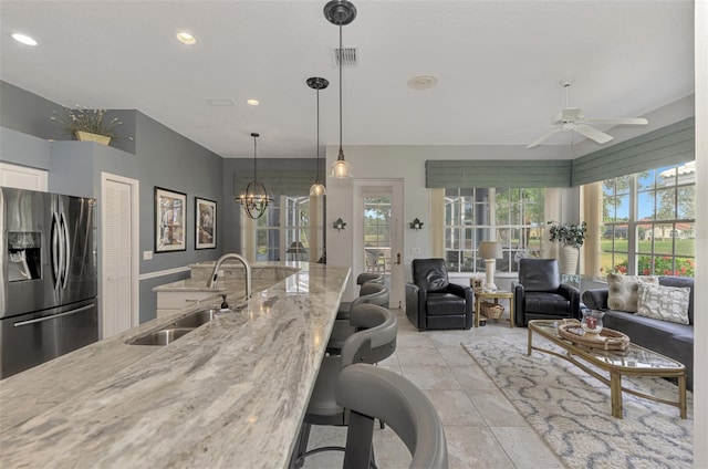 kitchen with pendant lighting, sink, light stone countertops, stainless steel fridge with ice dispenser, and ceiling fan with notable chandelier