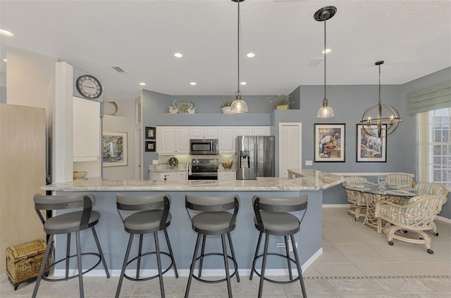 kitchen with appliances with stainless steel finishes, white cabinetry, an inviting chandelier, hanging light fixtures, and light stone counters