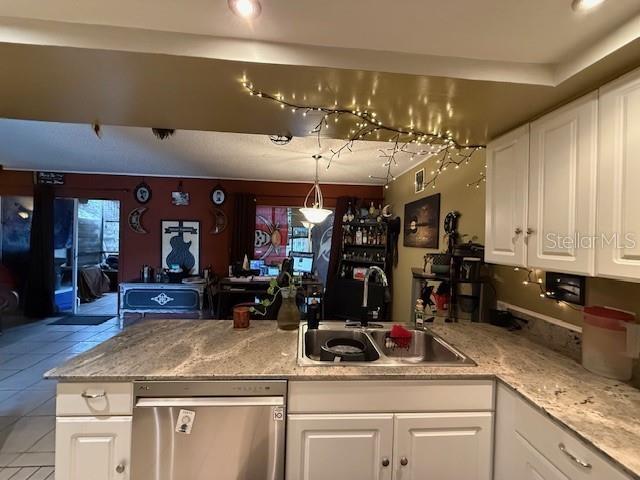 kitchen featuring light tile patterned floors, white cabinetry, kitchen peninsula, decorative light fixtures, and sink