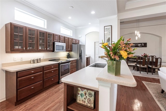 kitchen with sink, hanging light fixtures, light hardwood / wood-style flooring, ornamental molding, and appliances with stainless steel finishes