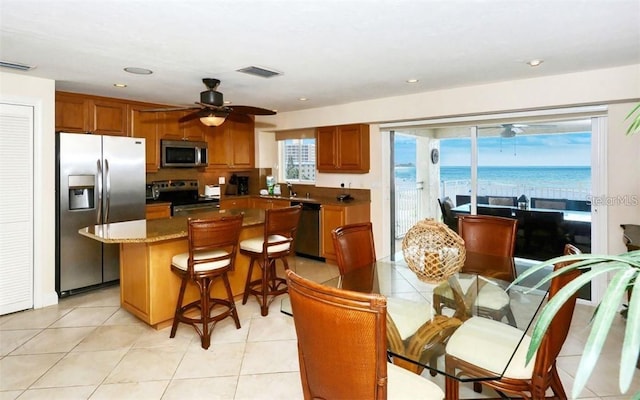 kitchen featuring a water view, visible vents, appliances with stainless steel finishes, brown cabinetry, and a kitchen island