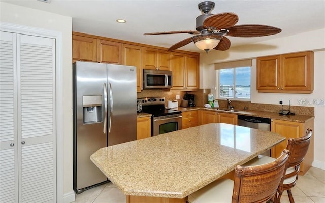 kitchen featuring a kitchen island, a breakfast bar area, light stone countertops, stainless steel appliances, and a sink