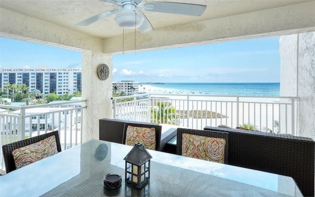 balcony with a beach view, outdoor dining space, a water view, and a ceiling fan