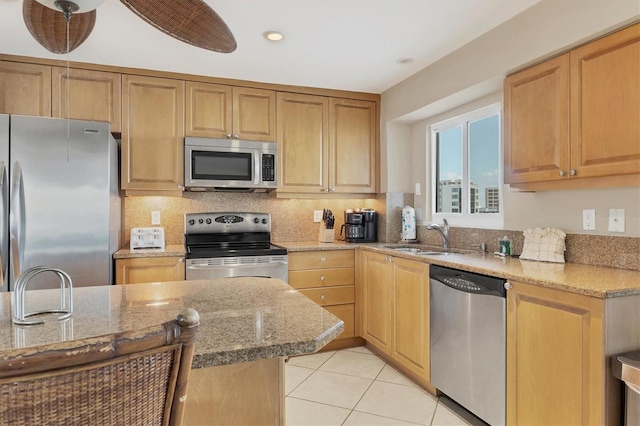 kitchen featuring stainless steel appliances, a sink, backsplash, and light stone counters