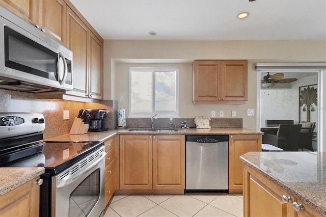 kitchen featuring light stone counters, light tile patterned flooring, stainless steel appliances, a sink, and tasteful backsplash