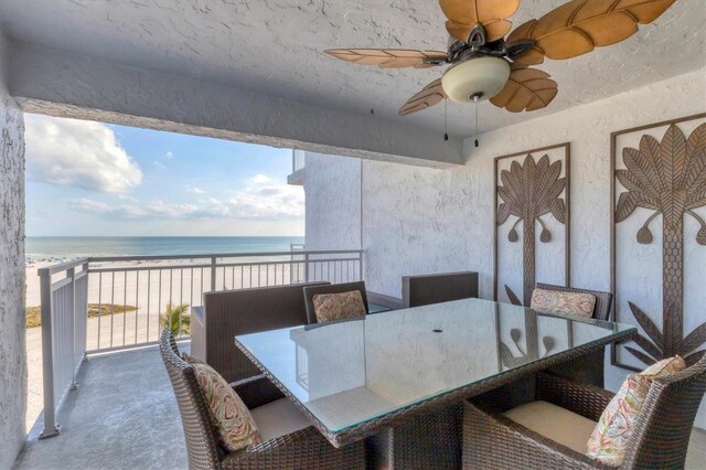 interior space with carpet, a view of the beach, a water view, a textured wall, and a ceiling fan