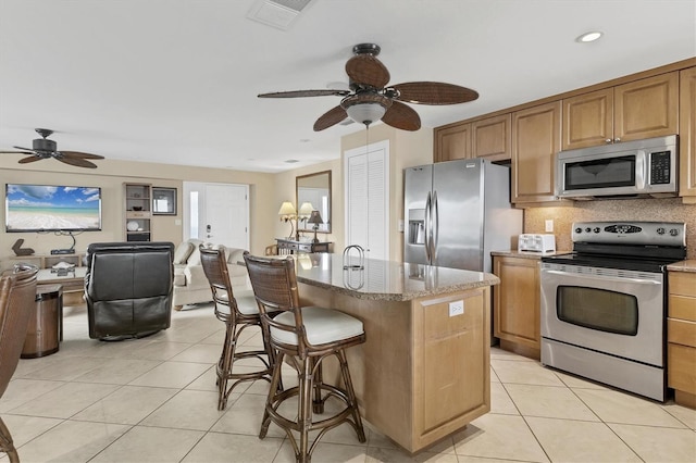 kitchen with light tile patterned floors, stainless steel appliances, visible vents, decorative backsplash, and a center island with sink