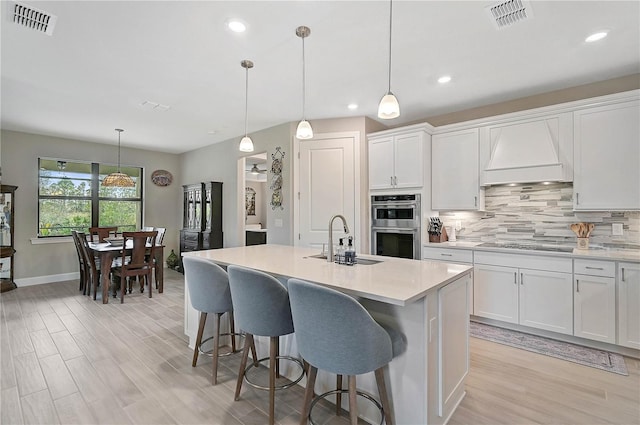 kitchen with custom exhaust hood, sink, white cabinetry, and pendant lighting