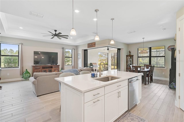 kitchen featuring white cabinets, dishwasher, an island with sink, sink, and a tray ceiling