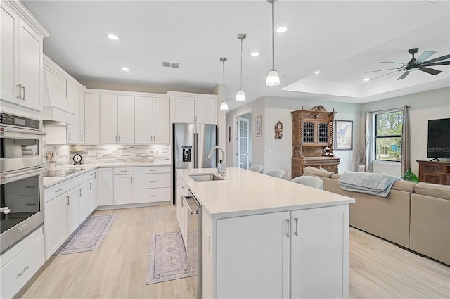 kitchen featuring white cabinets, decorative light fixtures, sink, a raised ceiling, and a center island with sink