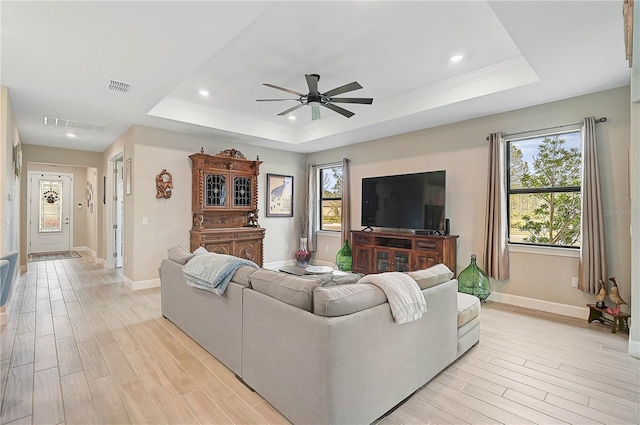 living room with a healthy amount of sunlight, light hardwood / wood-style floors, and a tray ceiling