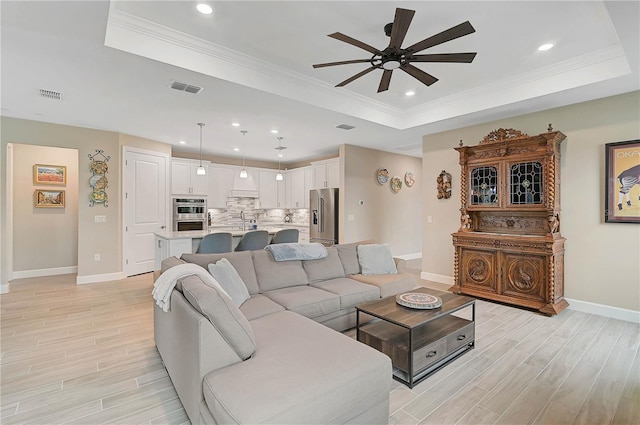 living room featuring ceiling fan, sink, a tray ceiling, and crown molding