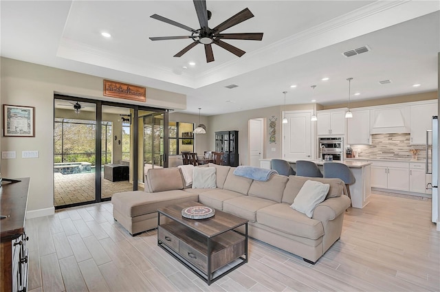 living room featuring ceiling fan, a tray ceiling, and crown molding