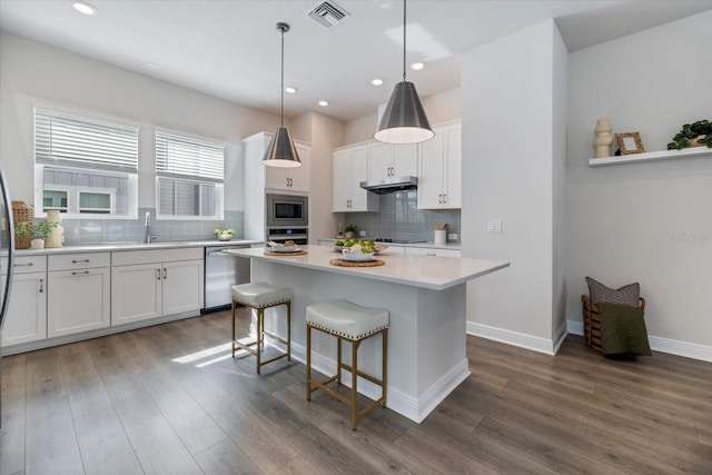 kitchen with tasteful backsplash, pendant lighting, a kitchen island, appliances with stainless steel finishes, and white cabinets