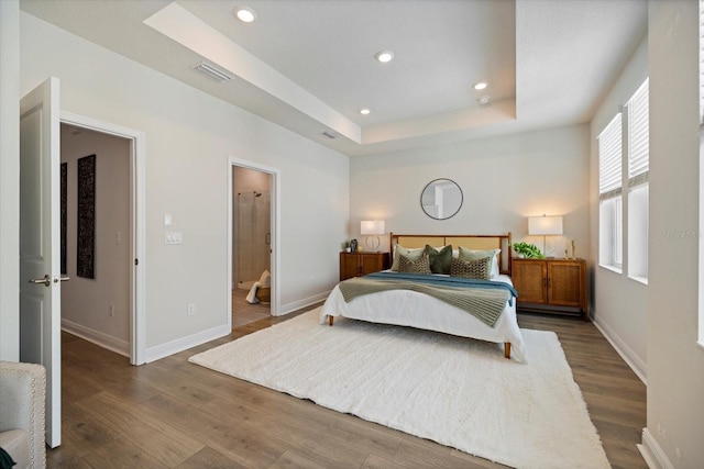 bedroom with ensuite bath, dark hardwood / wood-style floors, and a tray ceiling