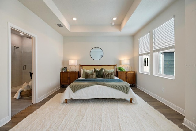 bedroom featuring ensuite bathroom, dark hardwood / wood-style floors, and a raised ceiling