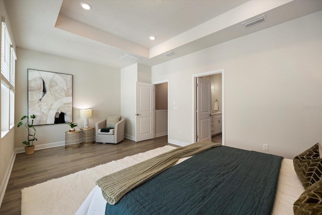 bedroom featuring ensuite bath, dark hardwood / wood-style floors, and a raised ceiling