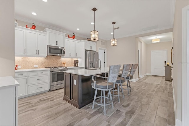 kitchen with white cabinetry, stainless steel appliances, tasteful backsplash, hanging light fixtures, and a kitchen island with sink