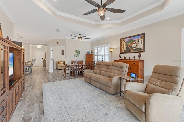 living room featuring a raised ceiling, ceiling fan, and ornamental molding