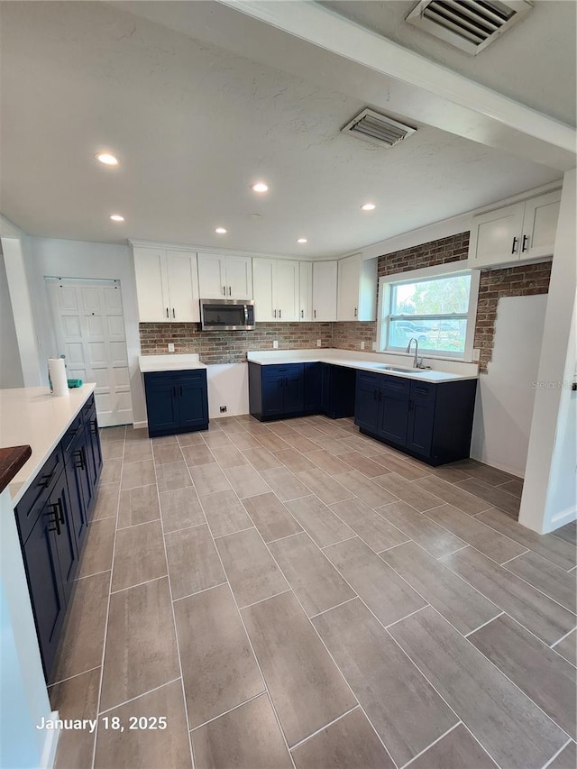 kitchen with white cabinetry, blue cabinets, backsplash, and sink