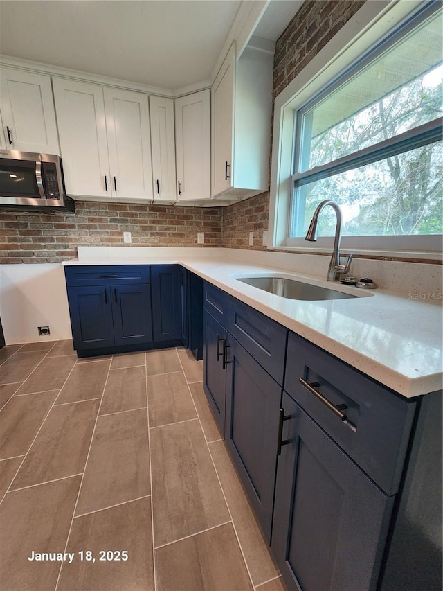 kitchen with brick wall, white cabinetry, blue cabinetry, and sink