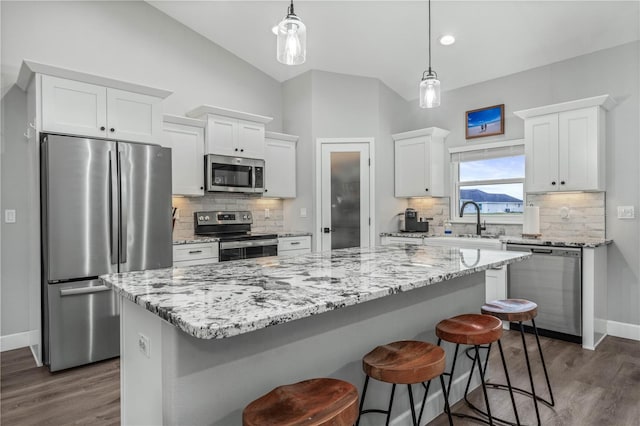 kitchen featuring white cabinets, appliances with stainless steel finishes, a center island, decorative light fixtures, and sink