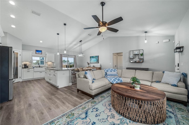 living room featuring ceiling fan, sink, lofted ceiling, and light wood-type flooring