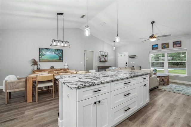 kitchen with vaulted ceiling, light hardwood / wood-style floors, pendant lighting, white cabinets, and light stone counters