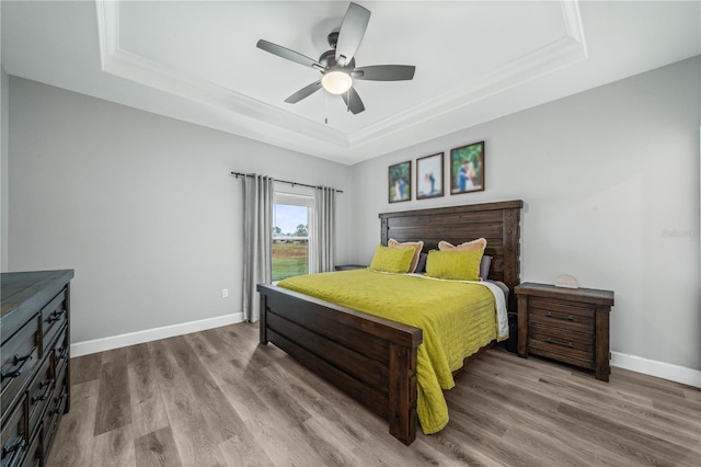 bedroom with a raised ceiling, ceiling fan, light wood-type flooring, and crown molding