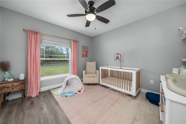 bedroom featuring ceiling fan, a nursery area, and hardwood / wood-style floors