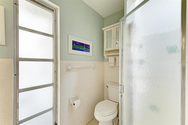 bathroom with tile walls, toilet, and a shower with door