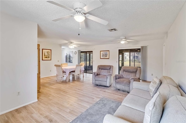 living room with ceiling fan, a textured ceiling, and light hardwood / wood-style flooring