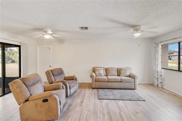 living room with light wood-type flooring, ceiling fan, and a textured ceiling