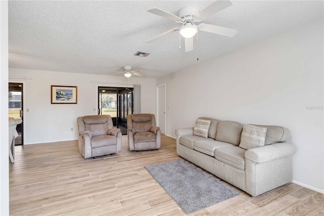 living room with ceiling fan, a textured ceiling, and light wood-type flooring