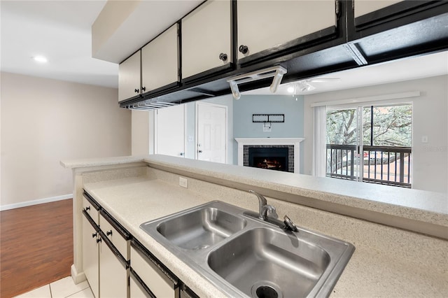 kitchen with a brick fireplace, sink, white cabinets, and light tile patterned flooring