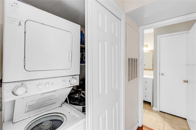 laundry area featuring light tile patterned floors and stacked washing maching and dryer