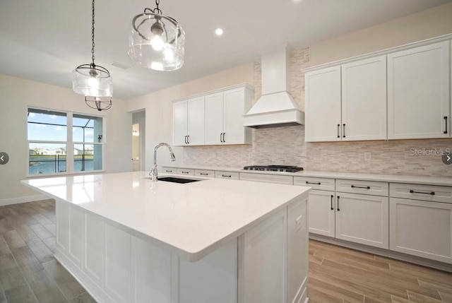 kitchen with hanging light fixtures, sink, custom range hood, and a center island with sink