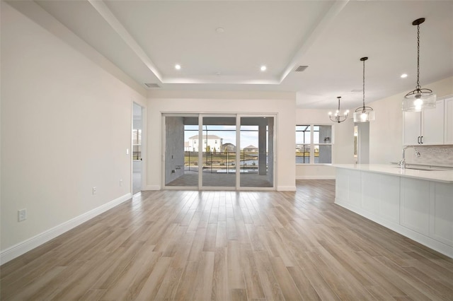unfurnished living room featuring light wood-style flooring, a tray ceiling, visible vents, baseboards, and recessed lighting
